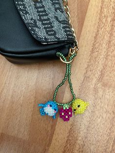 two colorful beads are attached to a black purse on a wooden floor next to a handbag