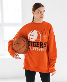 a woman holding a basketball in her right hand and wearing an orange sweatshirt with tigers on it