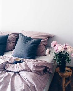 a bed with pink flowers in a black vase on top of it next to a white wall