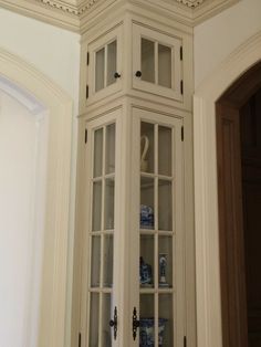 a tall white china cabinet in the corner of a room with glass doors and shelves