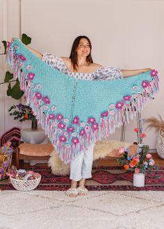 a woman standing in front of a rug holding a blue shawl with pink flowers on it