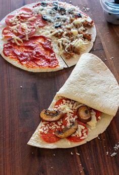 two pizzas with different toppings sitting on top of a wooden table next to each other