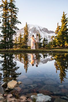 a bride and groom standing in front of a mountain lake with their reflection on the water