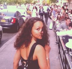 a woman standing in front of a row of parked cars on a street next to a crowd of people