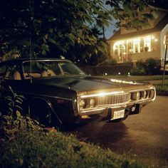 an old car parked in front of a house at night with lights on it's hood