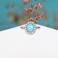 a close up of a ring on a table with flowers in the background and a blue backdrop