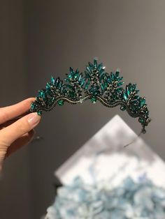 a hand holding a tiara with green beads