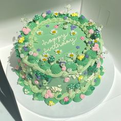 a green birthday cake decorated with flowers and leaves on a white tablecloth in a box