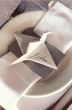 folded napkins and silverware on a white plate with an origami bird