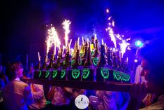 people are standing in front of a large display of bottles with fire on them at night