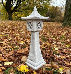 a stone lantern in the middle of leaves on the ground with trees and grass behind it