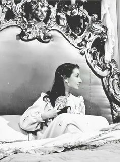 a woman sitting on top of a bed in front of a large mirror with an ornate frame