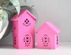 two pink paper houses sitting on top of a table next to a potted plant