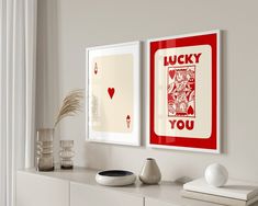 two red and white playing cards are hanging on the wall next to a vase with a plant in it