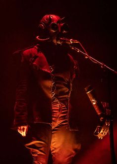 a man in a gas mask is on stage with a microphone and lights behind him