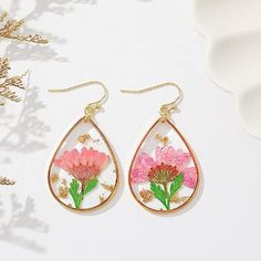 two pink flowers in tear shaped earrings on top of a white surface with gold ear wires