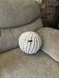 a white knitted ball sitting on top of a gray couch next to a brick wall