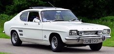 an old white car is parked on the side of the road in front of some trees