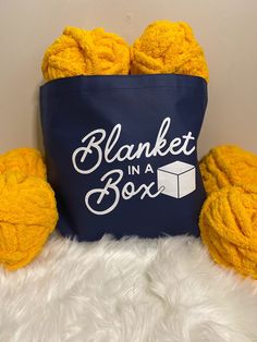 two balls of yarn sitting next to a blue bag that says blanket in a box