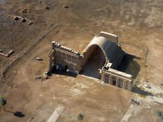 an aerial view of a large building in the middle of a desert area with trees and dirt