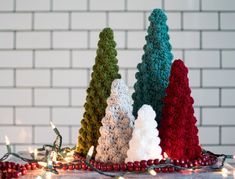 three crocheted christmas trees sitting on top of a table next to a white brick wall