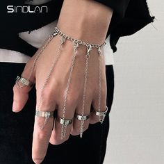 a person wearing silver chains and rings on their hands, with one hand holding the other