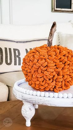 an orange pumpkin sitting on top of a white cake stand in front of a pillow