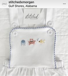 a white dress with fish embroidered on the front and bottom, along with an attached tag that says stitched morgan gulf shores, alabama