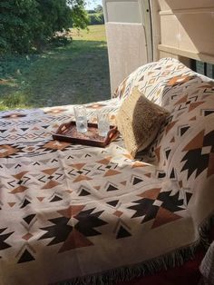 a bed sitting next to a window with a blanket on top of it and a pillow