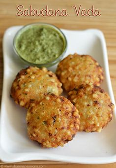 three crab cakes on a white plate with a small bowl of green sauce next to it