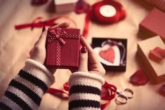 a person holding a small gift box with a red bow on it, surrounded by valentine's day decorations