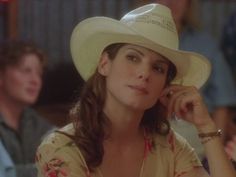 a woman wearing a white cowboy hat sitting at a table with other people in the background