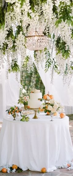 a table topped with a cake covered in white flowers next to a chandelier