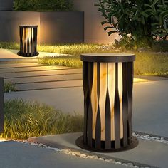 an outdoor lamp is lit up on the ground next to some grass and bushes at night