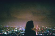 a person standing in front of a cityscape at night with the lights on