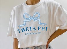 a woman wearing a white t - shirt with a blue bow on the front that says,'thea phi established 1971 '