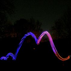 a long exposure photo of light painting in the dark with trees and sky behind it