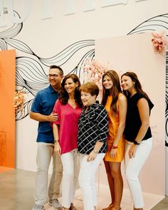 a group of people standing next to each other in front of a wall with flowers