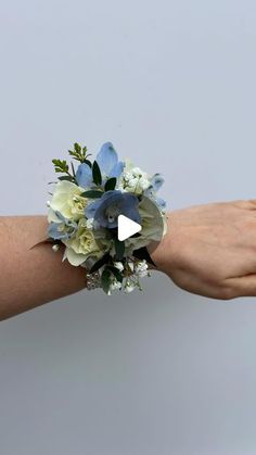 a woman's hand holding a bouquet of white and blue flowers on her wrist