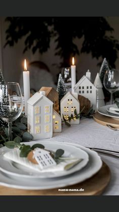 the table is set with white plates and silverware, candles and greenery on it