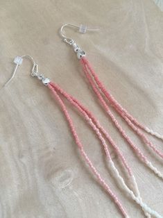 pink and white beads are hanging from silver earwires on a beige cloth background