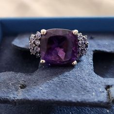 5.50 Carat Amethyst And .40 Ct. T.W. Tanzanite Ring In Sterling Silver 5.50 Carat Amethyst And .40 Ct. T.W. Tanzanite Ring In Sterling Silver. Size 7 Sizable This Ring Is All About Royal Hues. A 5.50 Carat Cushion-Cut Amethyst Is Centered Between Clusters Of Tanzanite Rounds Totaling .40 Carats. Black Rhodium. Set In Sterling Silver. 1/2" Wide. Tanzanite And Amethyst Ring Formal Purple Sapphire Ring With Gemstone Accents, Elegant Purple Sapphire Ring With Gemstone Accents, Elegant Purple Ring With Center Stone, Elegant Purple Sapphire Ring With Center Stone, Purple Ring With Gemstone Accents For Formal Occasions, Elegant Amethyst Gemstones With Accent Stones, Luxury Purple Multi-stone Sapphire Ring, Purple Multi-stone Amethyst Ring In Fine Jewelry Style, Purple Diamond Rings With Accent Stones