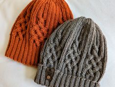 two knitted hats laying on top of each other, one is orange and the other is gray