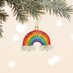 a christmas ornament hanging from a tree with a rainbow in the middle and snow around it