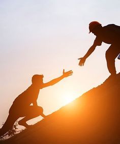 two people on top of a hill reaching out to each other with their hands as the sun sets behind them