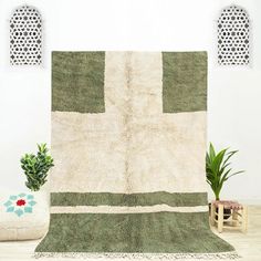 a green and white rug sitting on top of a wooden floor next to a potted plant