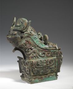 an old metal object with carvings on the top and bottom, sitting in front of a gray background