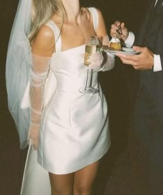 a man and woman in wedding attire standing next to each other holding plates with food on them