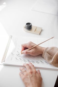 a woman is writing on a notebook with a pencil in her left hand and an ink pen in her right hand