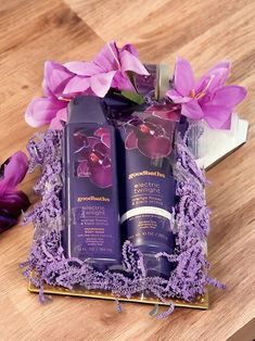 two bottles of body lotion sitting on top of a wooden table next to purple flowers